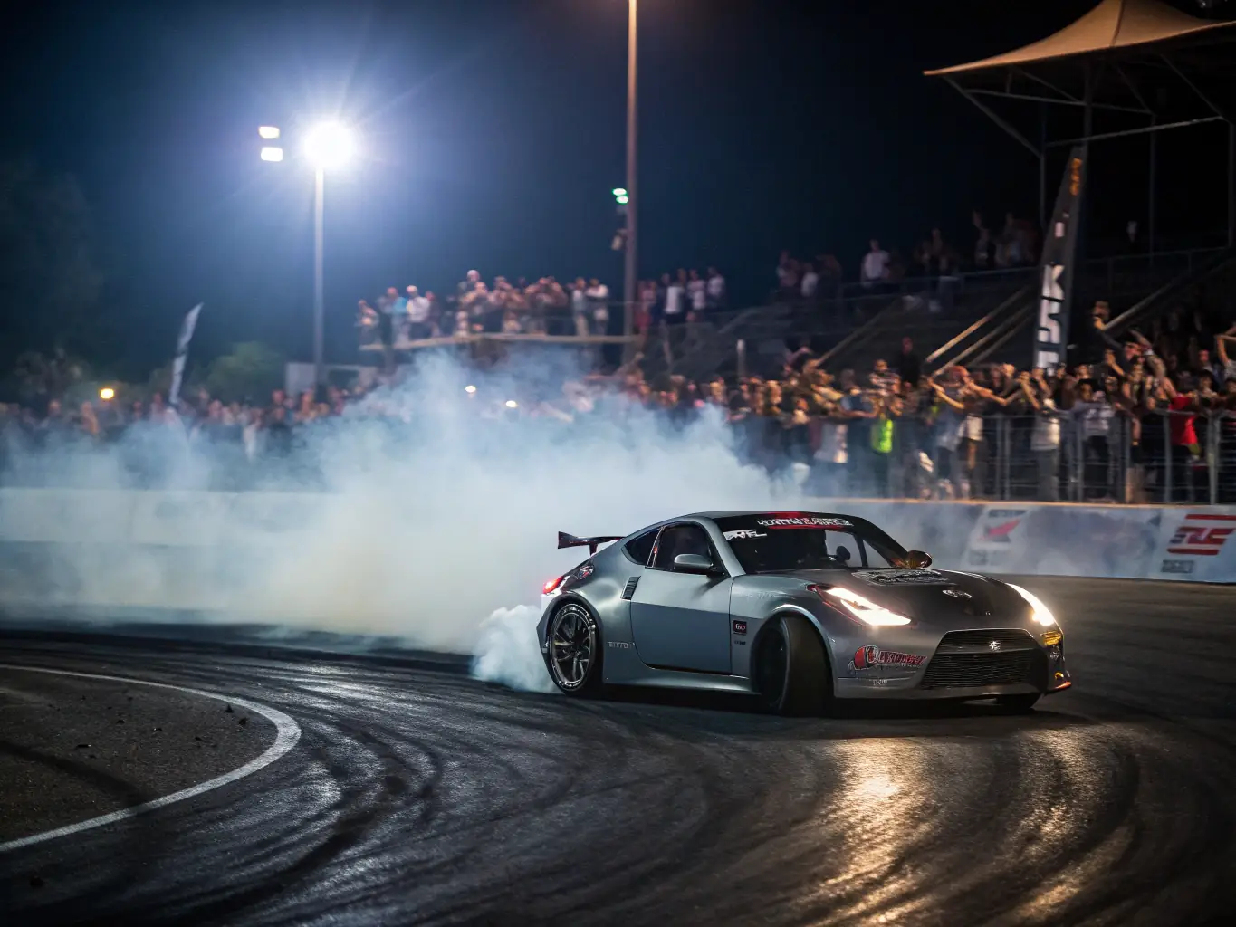 A dynamic image of a JAPAN DAYS motorsport event, featuring a high-performance Japanese car drifting on a track, surrounded by cheering spectators and event staff.